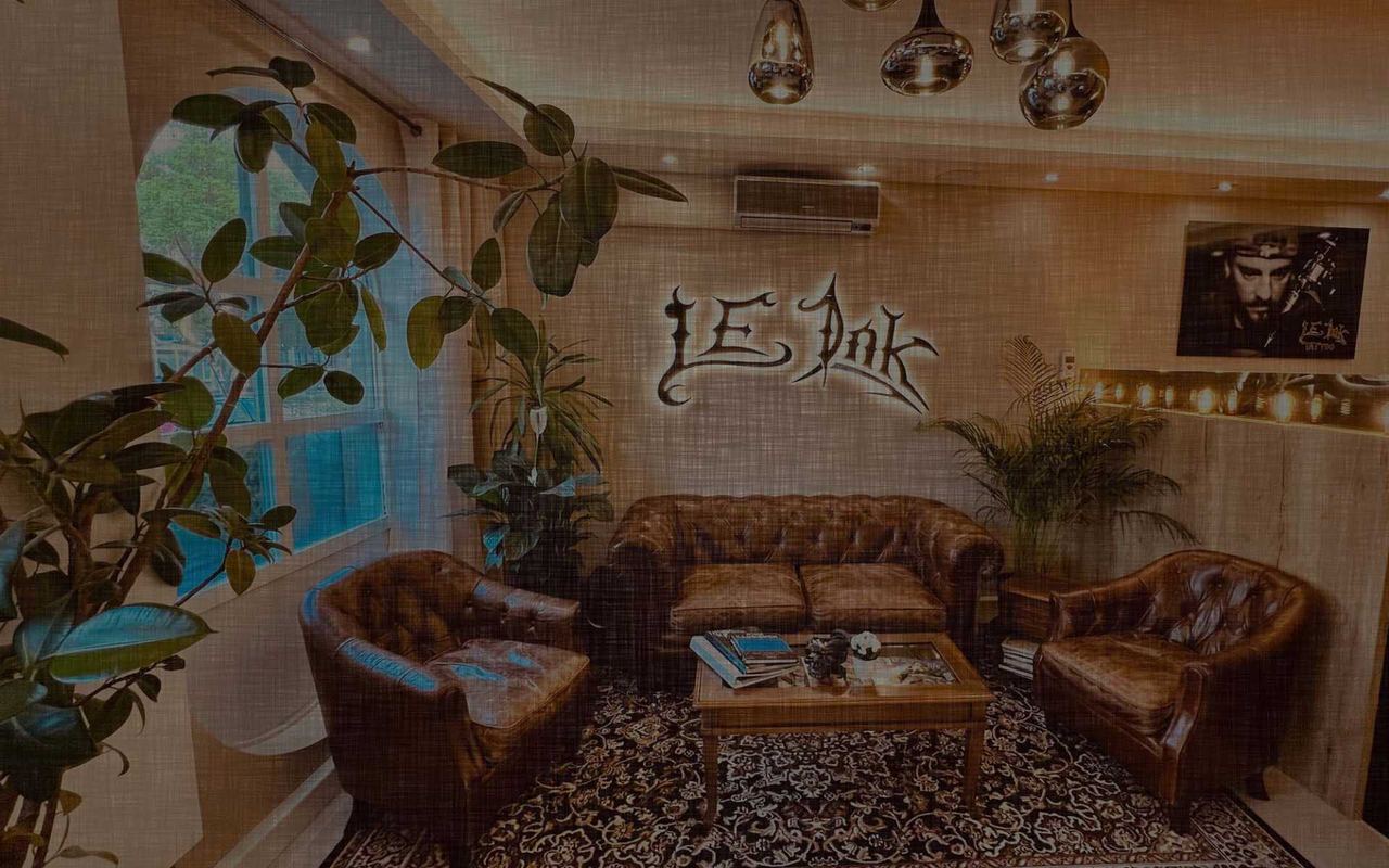Lounge im LE Ink Tattoo-Studio mit Chesterfield-Sofas, Pflanzen und dem LE-Ink-Logo an der Wand