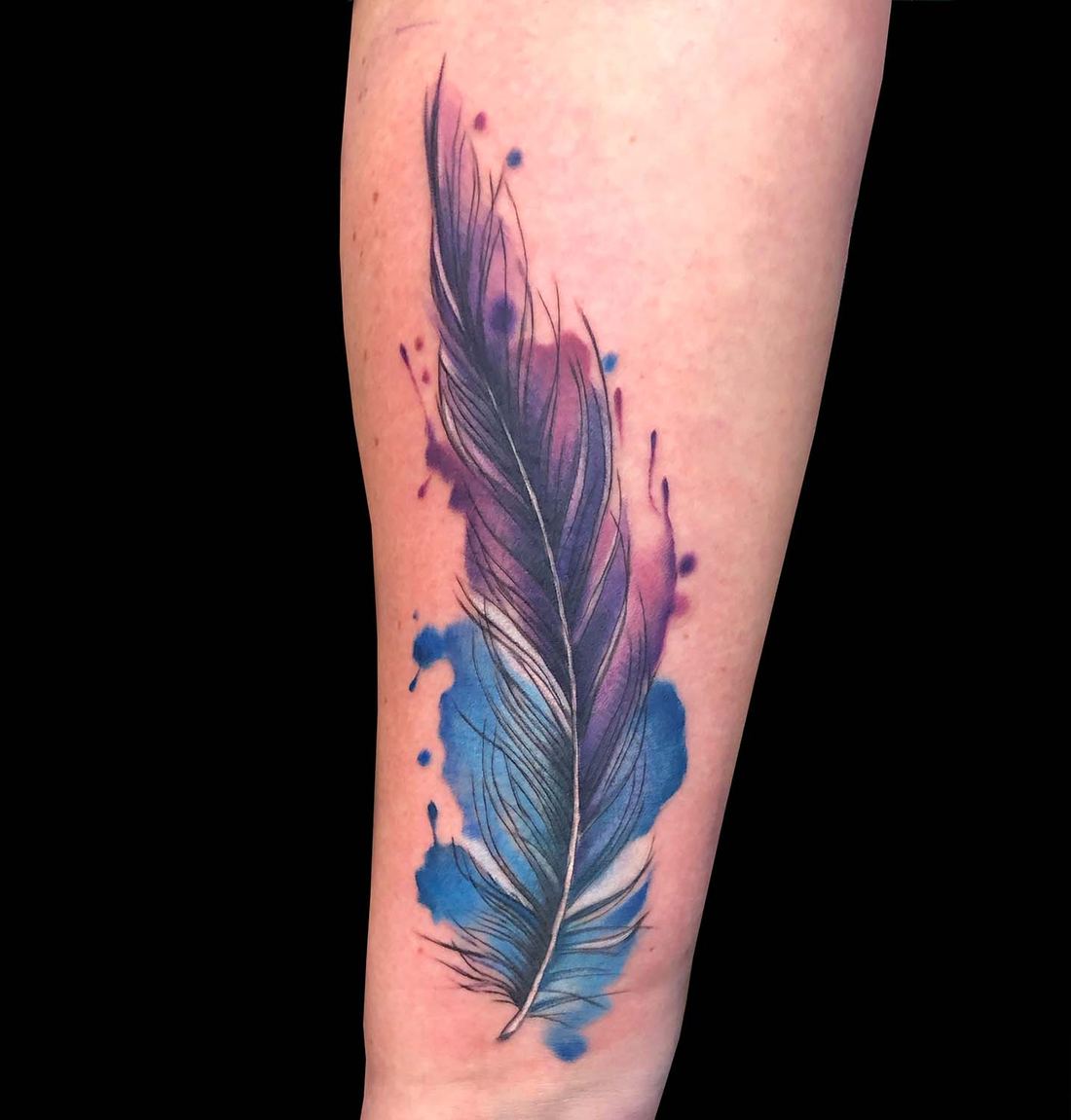 Feder in Blau- und Violetttönen am Unterarm